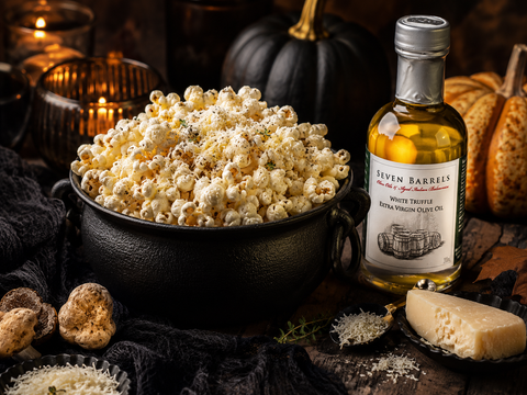 White truffle Parmesan popcorn in a black cauldron with Seven Barrels White Truffle Extra Virgin Olive Oil in a moody Halloween setting