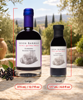 Two bottles of Seven Barrels Elderberry Balsamic Vinegar shown outdoors on a stone surface, with a large bottle labeled Large (375 mL / 12.7 fl oz) and a smaller bottle labeled Small (177 mL / 6.
