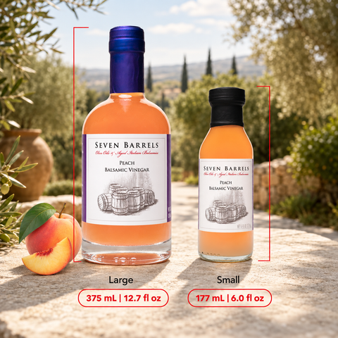 Two bottles of Seven Barrels Peach Balsamic Vinegar shown outdoors on a stone surface, labeled Large (375 mL / 12.7 fl oz) and Small (177 mL / 6.