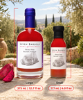Two bottles of Seven Barrels Picky Pear Balsamic Vinegar shown outdoors on a stone surface, with a large bottle labeled Large and a smaller bottle labeled Small. Red measurement lines and text indicate the sizes and volumes.